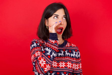 Photo for Brunette caucasian woman wearing christmas sweater over red background hear incredible private news impressed scream share - Royalty Free Image