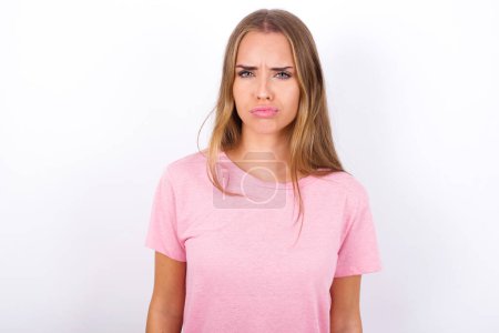 Téléchargez les photos : Offensé insatisfait Jeune fille caucasienne portant T-shirt rose sur fond blanc avec expression mécontente lunatique à la caméra être déçu par quelque chose - en image libre de droit