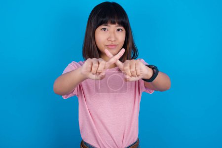 Photo for Young asian woman wearing pink t-shirt against blue background has rejection angry expression crossing fingers doing negative sign. - Royalty Free Image