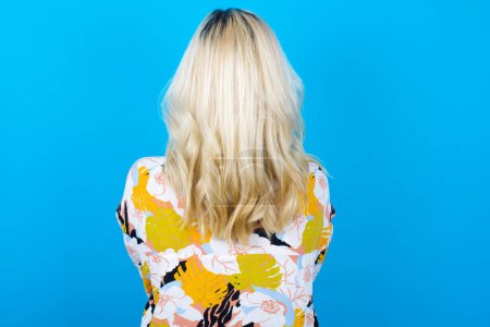 Photo for Caucasian girl wearing floral shirt isolated over blue background standing backwards looking away with arms on body. - Royalty Free Image