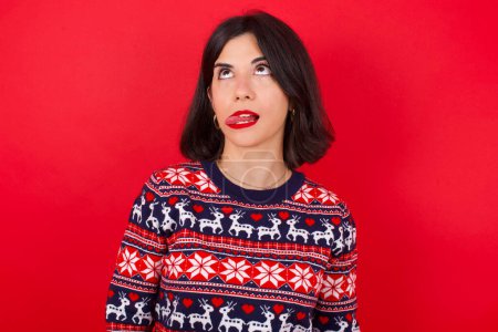 Photo for Brunette caucasian woman wearing christmas sweater over red background showing grimace face crossing eyes and showing tongue. Being funny and crazy - Royalty Free Image