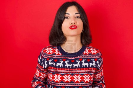 Photo for Brunette caucasian woman wearing christmas sweater over red background making fish face with lips, crazy and comical gesture. Funny expression. - Royalty Free Image