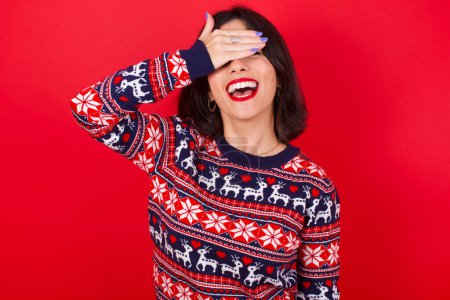 Photo for Brunette caucasian woman wearing christmas sweater over red background smiling and laughing with hand on face covering eyes for surprise. Blind concept. - Royalty Free Image