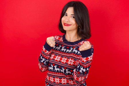 Photo for Brunette caucasian woman wearing christmas sweater over red background Ready to fight with fist defense gesture, angry and upset face, afraid of problem. - Royalty Free Image