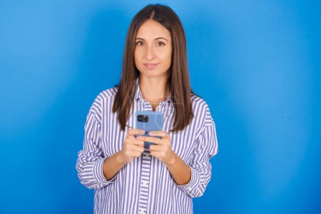 Téléchargez les photos : Portrait de sérieux confiant jeune femme tenant le téléphone dans les deux mains - en image libre de droit