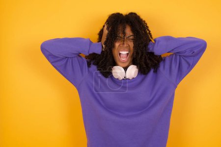 Foto de Retrato de joven mujer afroamericana expresiva con auriculares sobre fondo amarillo - Imagen libre de derechos