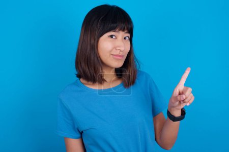 Photo for No sign gesture. Closeup portrait unhappy young asian woman wearing blue t-shirt against blue background raising fore finger up saying no. Negative emotions facial expressions, feelings. - Royalty Free Image