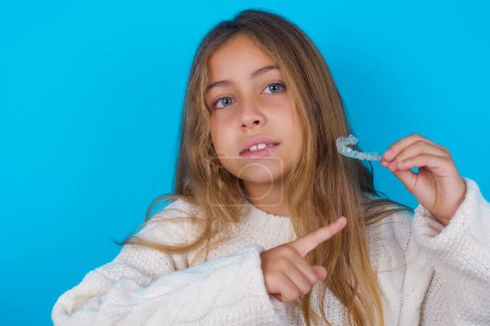 Foto de Bonita adolescente sosteniendo un alineador invisible y señalándolo. Salud dental y concepto de confianza. - Imagen libre de derechos