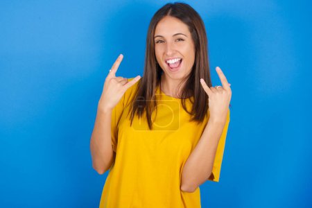 Photo for Beautiful young woman makes rock n roll sign looks self confident and cheerful enjoys cool music at party. Body language concept. - Royalty Free Image