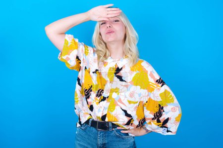 Photo for Caucasian girl wearing floral shirt isolated over blue background wiping forehead with hand making phew gesture, expressing relief feels happy that he prevented huge disaster. It was close enough - Royalty Free Image