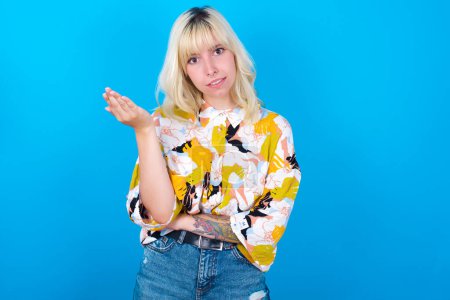 Téléchargez les photos : Studio shot of frustrated Caucasian girl wearing floral shirt isolated over blue background gesturing with raised palm, frowning, being displeased and confused with dumb question. - en image libre de droit