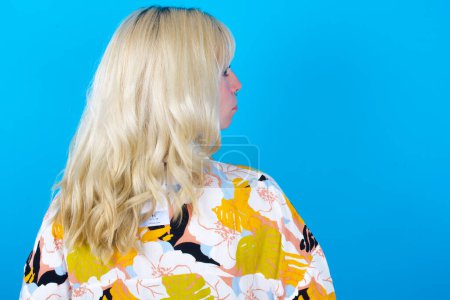 Photo for The back view of caucasian girl wearing floral shirt isolated over blue background. Studio Shoot. - Royalty Free Image