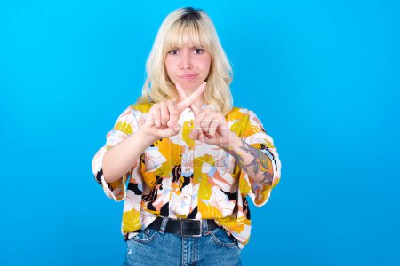 Photo for Caucasian girl wearing floral shirt isolated over blue background has rejection angry expression crossing fingers doing negative sign. - Royalty Free Image