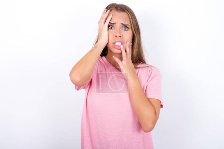 Junge düstere junge kaukasische Mädchen tragen rosa T-Shirt auf weißem Hintergrund verbergen Gesicht mit Händen schmollen und weinen, stehen aufgebracht und deprimiert jammert über Arbeitsplatzproblem.