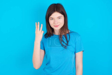Photo for Young caucasian girl wearing blue t-shirt isolated over blue studio background smiling and looking friendly, showing number three or third with hand forward, counting down - Royalty Free Image