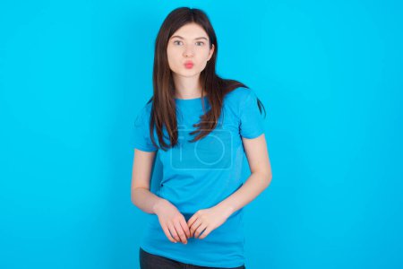 Téléchargez les photos : Portrait de belle jeune fille caucasienne drôle portant t-shirt bleu isolé sur fond de studio bleu envoyer baiser d'air - en image libre de droit