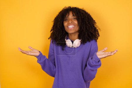 portrait of young expressive african american woman with headphones on yellow background shredding shoulders