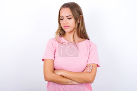 Téléchargez les photos : Mécontent Jeune fille caucasienne portant un T-shirt rose sur fond blanc avec une mauvaise attitude, les bras croisés regardant de côté. Émotion humaine négative sentiments d'expression faciale. - en image libre de droit