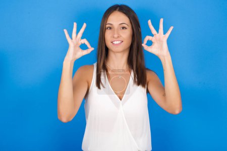 Photo for Glad beautiful young woman shows ok sign with both hands as expresses approval, has cheerful expression, being optimistic. - Royalty Free Image