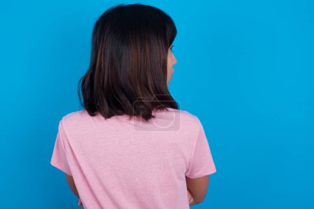 Photo for The back view of young asian woman wearing pink t-shirt against blue background Studio Shoot. - Royalty Free Image