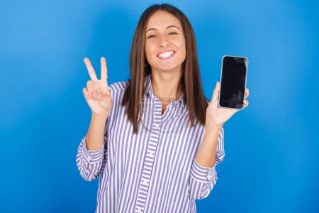 Téléchargez les photos : Belle jeune femme tenant dispositif moderne montrant v-signe - en image libre de droit