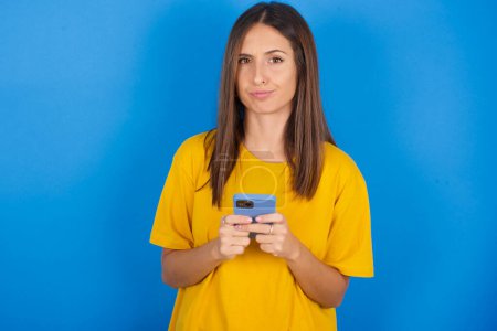 Photo for Portrait of a confused beautiful young woman holding mobile phone and shrugging shoulders and frowning face. - Royalty Free Image