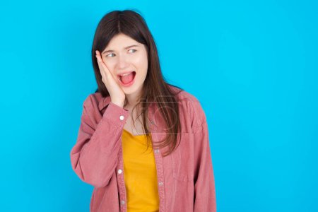 Photo for Young caucasian girl wearing pink shirt isolated over blue background excited looking to the side hand on face. Advertisement and amazement concept. - Royalty Free Image