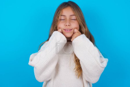Photo for Pleased pretty teen girl with closed eyes keeps hands near cheeks and smiles tenderly imagines something very pleasant - Royalty Free Image