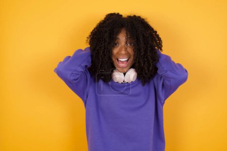 Téléchargez les photos : Portrait de jeune femme afro-américaine expressive avec écouteurs sur fond jaune - en image libre de droit
