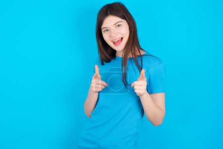 Foto de Joven chica caucásica con camiseta azul aislado sobre fondo estudio azul dirige los dedos a la cámara selecciona a alguien. Te recomiendo. La mejor opción - Imagen libre de derechos