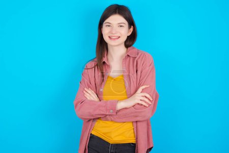 Téléchargez les photos : Jeune fille caucasienne portant chemise rose isolé sur fond bleu étant heureux souriant et les bras croisés regardant avec confiance à la caméra. Personne positive et confiante. - en image libre de droit