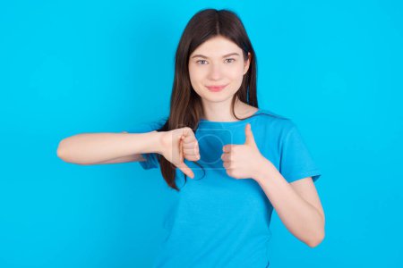 Photo for Young caucasian girl wearing blue t-shirt isolated over blue studio background showing thumb up down sign - Royalty Free Image