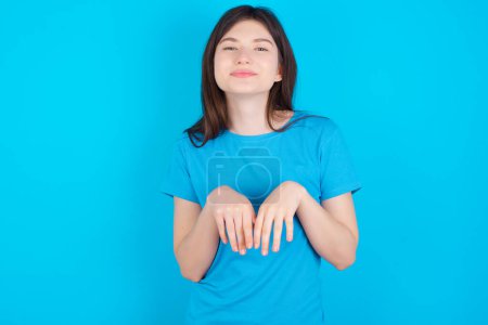 Foto de Joven caucásico chica usando azul camiseta aislado sobre azul estudio fondo hace conejito patas y miradas con inocente expresión juega con su pequeño niño - Imagen libre de derechos