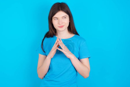 Photo for Young caucasian girl wearing blue t-shirt isolated over blue studio background steepls fingers and looks mysterious aside has great evil plan in mind - Royalty Free Image