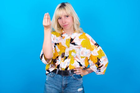 Foto de What the hell are you talking about. Shot of frustrated caucasian girl wearing floral shirt isolated over blue background gesturing with raised hand doing Italian gesture, frowning, being displeased and confused with dumb question. - Imagen libre de derechos