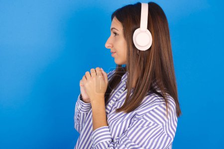 Beautiful young woman wears stereo headphones listening to music concentrated and looking aside with interest.
