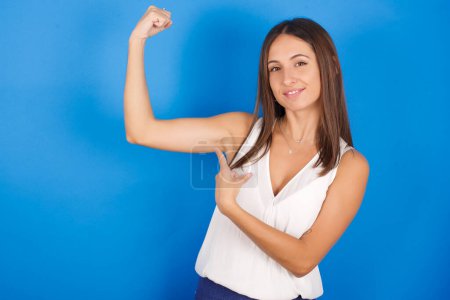 Photo for Smiling beautiful young woman raises hand to show muscles, feels confident in victory, strong and independent. - Royalty Free Image