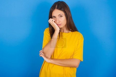 Photo for Very bored beautiful young woman holding hand on cheek while support it with another crossed hand, looking tired and sick. - Royalty Free Image
