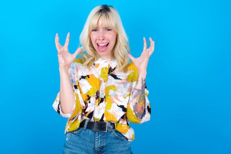 Photo for Caucasian girl wearing floral shirt isolated over blue background crying and screaming. Human emotions, facial expression concept. Screaming, hate, rage. - Royalty Free Image