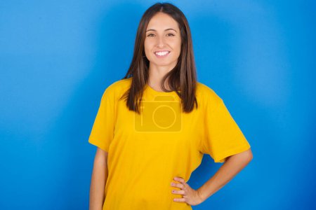Photo for Studio shot of cheerful pretty girl keeps hand on hip, smiles broadly. - Royalty Free Image