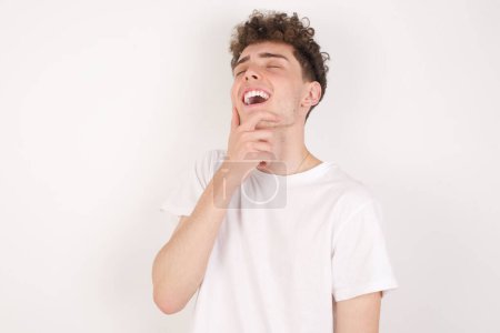 Photo for Handsome young man laughs happily keeps hand on chin expresses positive emotions smiles broadly has carefree expression - Royalty Free Image