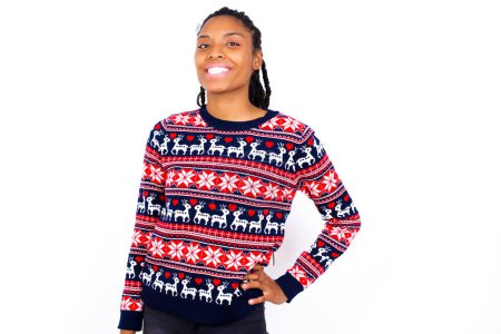 Photo for Studio shot of cheerful African American woman wearing Christmas sweater against white wall keeps hand on hip, smiles broadly. - Royalty Free Image