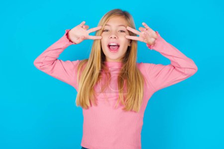 Photo for Cheerful positive pretty teen girl shows v-sign near eyes open mouth - Royalty Free Image