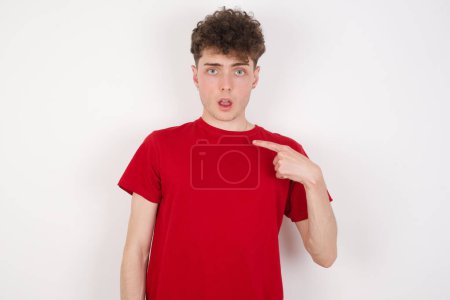 Photo for Handsome young man being in stupor shocked, has astonished expression pointing at oneself with finger saying: Who me? - Royalty Free Image