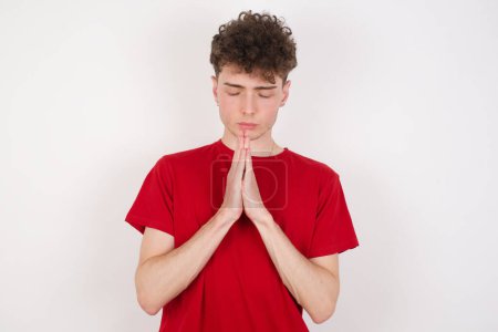 Indoor closeup of handsome young man practicing yoga and meditation, holding palms together in namaste, looking calm, relaxed and peaceful.