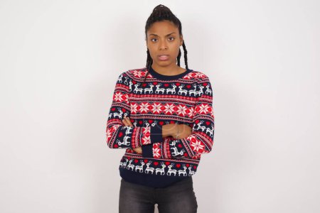 Photo for African American woman wearing Christmas sweater against white wall frowning his face in displeasure, keeping arms folded, waiting for an explanation. - Royalty Free Image