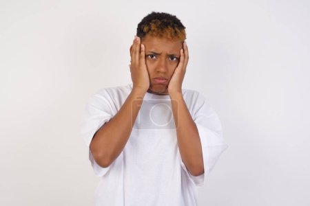 Photo for Portrait of beautiful young african-american woman wearing white t-shirt holding head in hands with unhappy expression watching sad movie about animals and trying not to cry. - Royalty Free Image