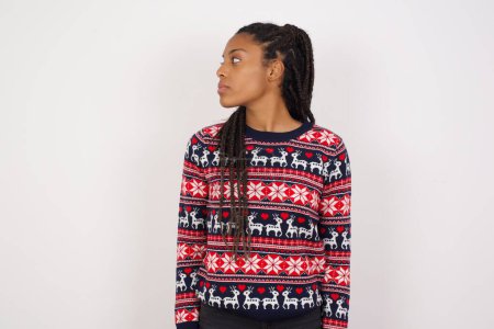 Photo for Side view of young happy smiling African American woman wearing Christmas sweater against white wall - Royalty Free Image