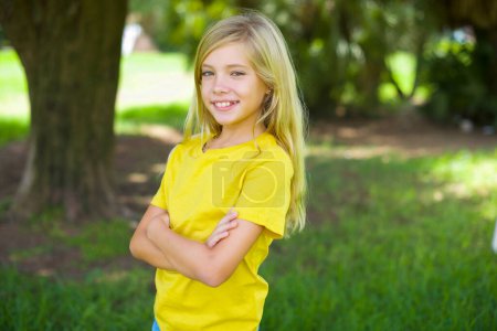Photo for Portrait of caucasian little girl wearing yellow t-shirt standing outdoors standing with folded arms and smiling - Royalty Free Image