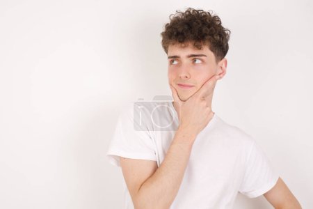 Photo for Thoughtful handsome young man holds chin and looks away pensively makes up great plan - Royalty Free Image